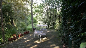 A garden patio with a metal table and chairs, surrounded by lush greenery and trees. - Castello di Montalto - La Scuola (Castelnuovo Berardenga)