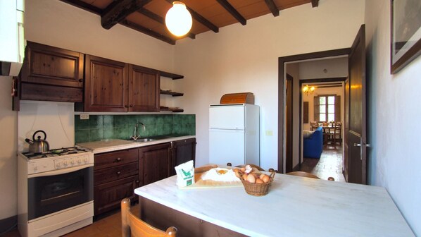 A kitchen with wooden cabinets, a gas stove, a refrigerator, and a marble countertop with a basket of eggs.