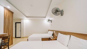 Een hotelkamer met twee bedden, een houten garderobe, een bureau met stoel en een ventilator aan de muur.