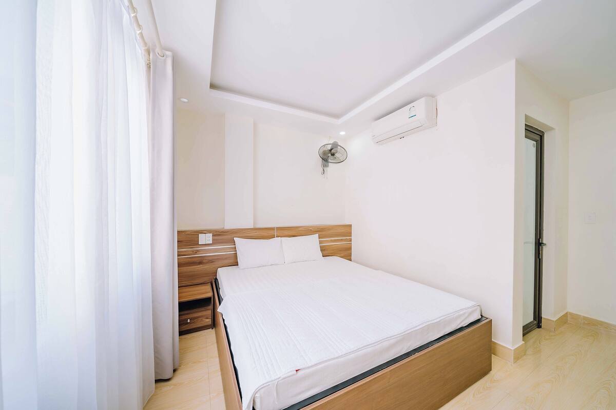 Een slaapkamer met een houten bed, witte beddengoed, een plafondventilator en een airconditioning.