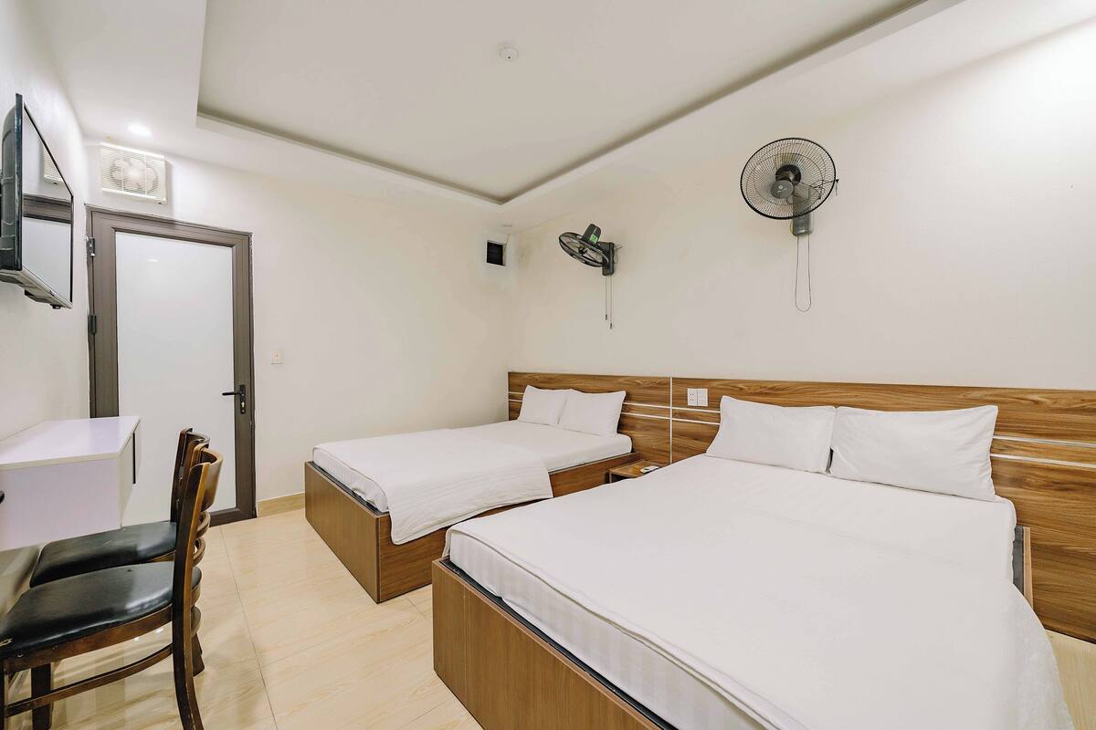 Een hotelkamer met twee eenpersoonsbedden, een bureau, een stoel, een ventilator aan de muur en een plafondventilator.