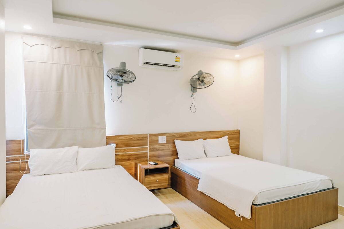Een hotelkamer met twee enkele bedden, een houten hoofdbord, een nachtkastje en twee wandventilatoren.