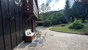 Una edificación de madera con porche, patio de ladrillo y vista a un área boscosa.
