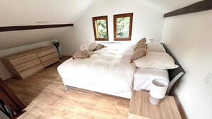 Un dormitorio con cama, mesitas de noche, cómoda y dos ventanas.