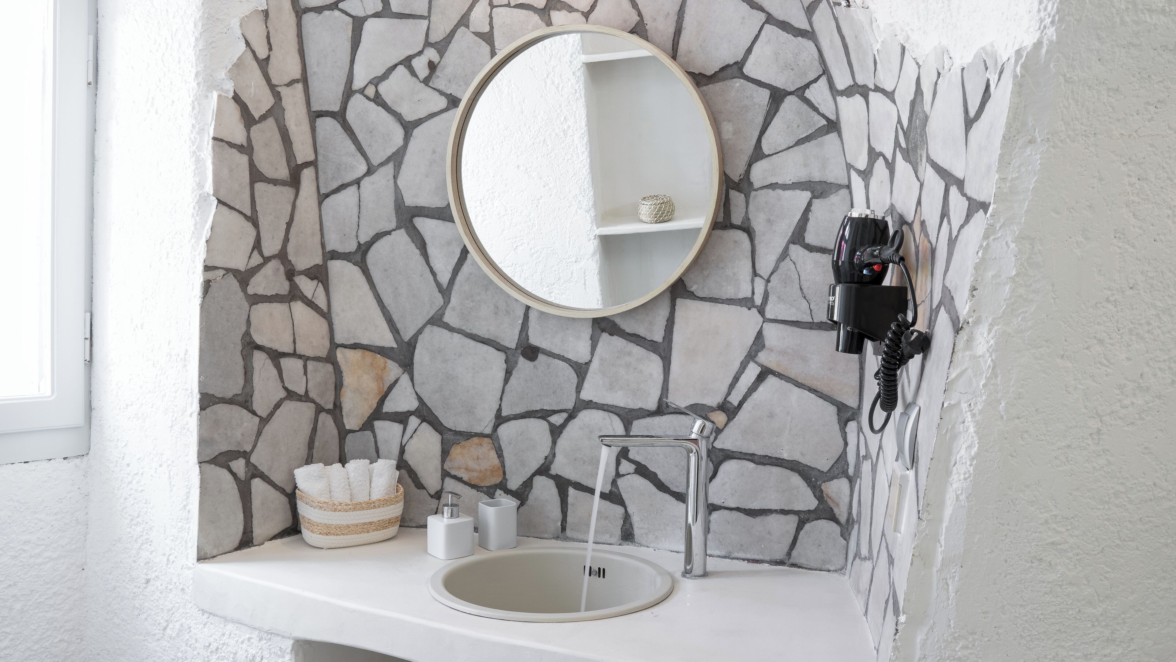 A bathroom with a stone wall, a round mirror, a sink, and a towel rack.