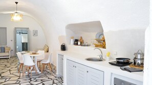 A compact kitchen with a white countertop, a sink, and a stove. There is a dining area with a table and chairs. - Modern traditional cave home, close to Fira, port and airport! (Santorini)