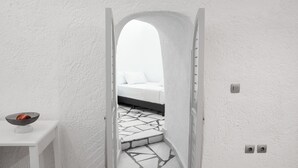 Ein schmaler Flur, der in ein Schlafzimmer mit einem Bett, einem kleinen Tisch mit einer Schüssel und einem gefliesten Boden führt.