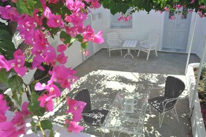 A patio with white furniture, including two chairs and a table, surrounded by pink flowers. - Modern traditional cave home, close to Fira, port and airport! (Santorini)