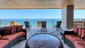 A balcony with wicker furniture, a round table, and a view of the ocean.