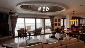 A spacious living room with a large sectional sofa, a fireplace, and a view of the ocean through large windows.