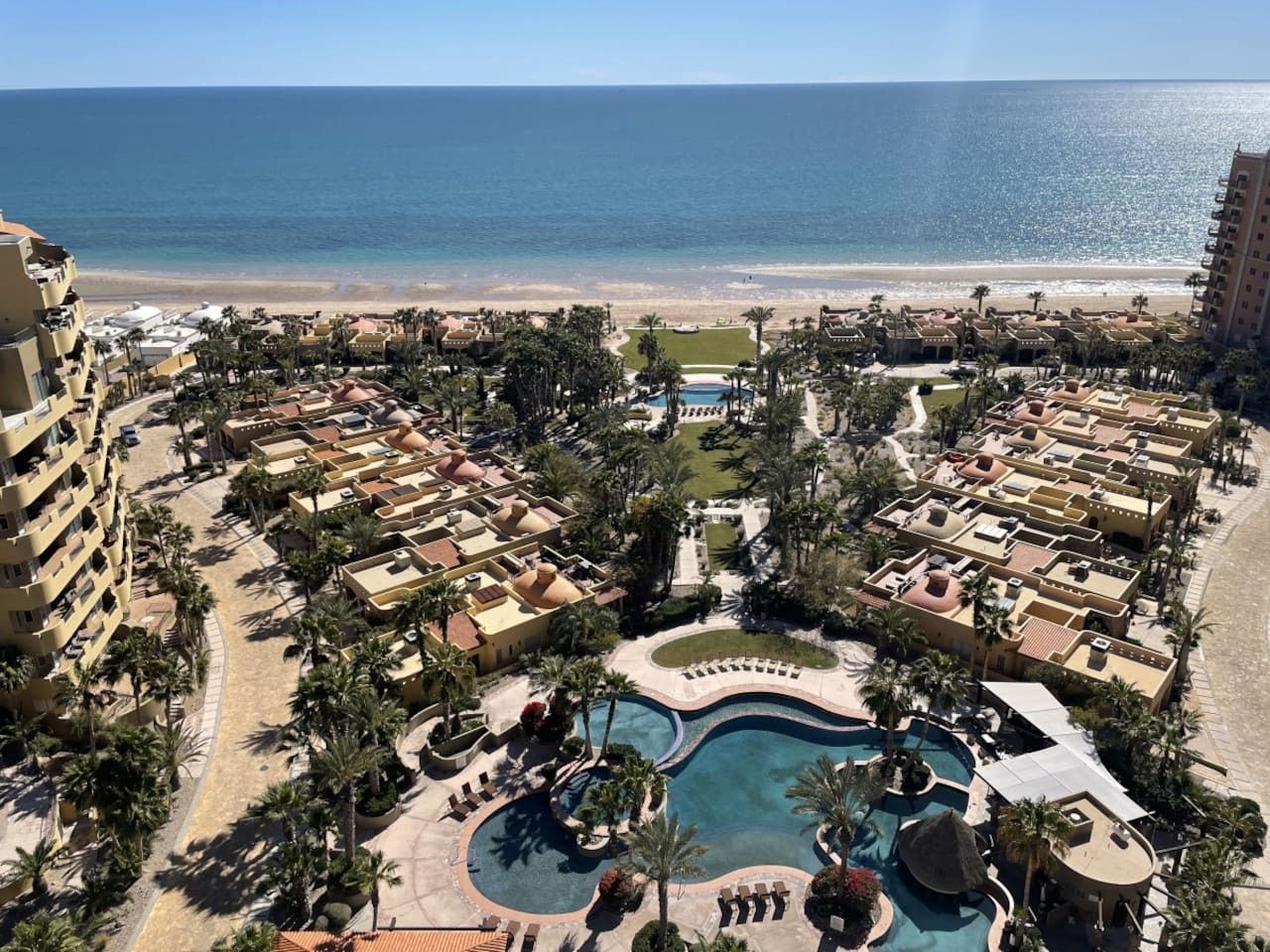 A resort with a central pool, beachfront villas, and a view of the ocean.