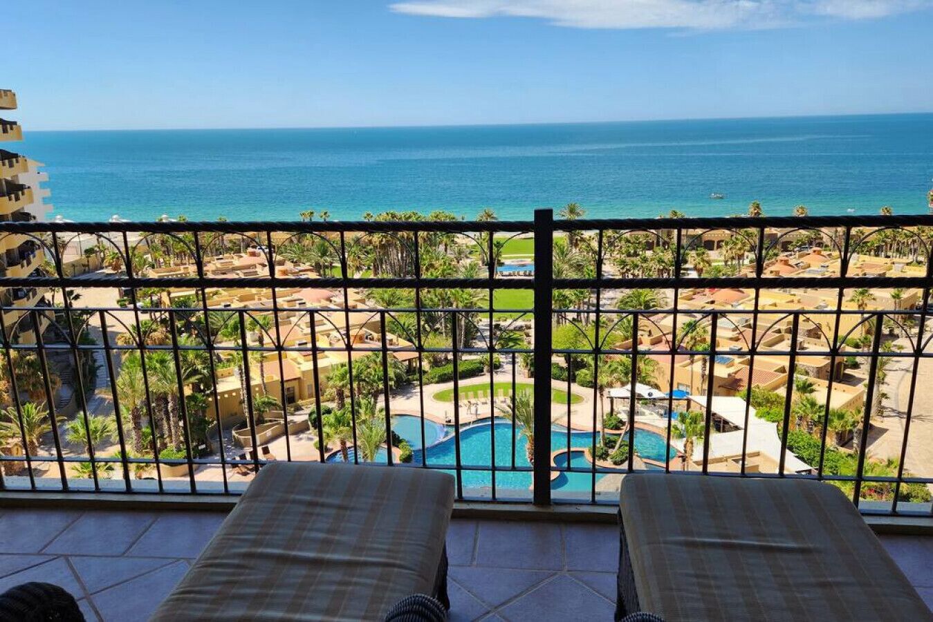 A balcony with two lounge chairs overlooking a pool and a view of the ocean.