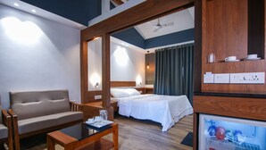 A hotel room with a sofa, a bed, a coffee table, a minibar, and a ceiling fan. - B'camp Resorts & Homestays (Vythiri)