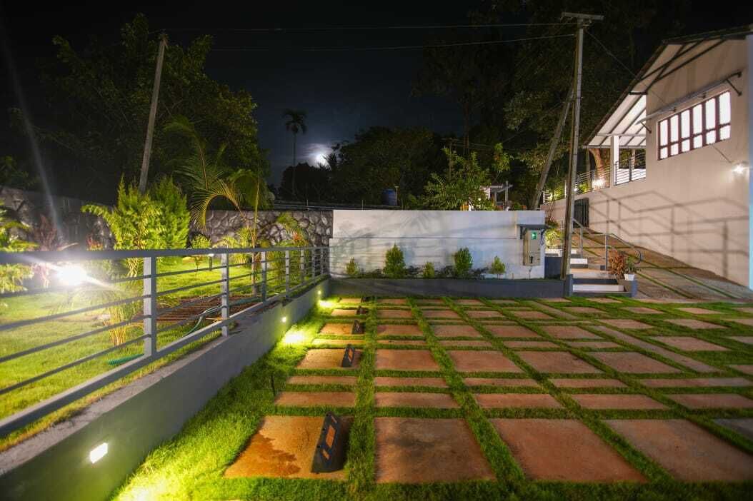 Un espacio exterior bien iluminado con un sendero pavimentado, una fuente pequeña y un edificio blanco con ventanas.