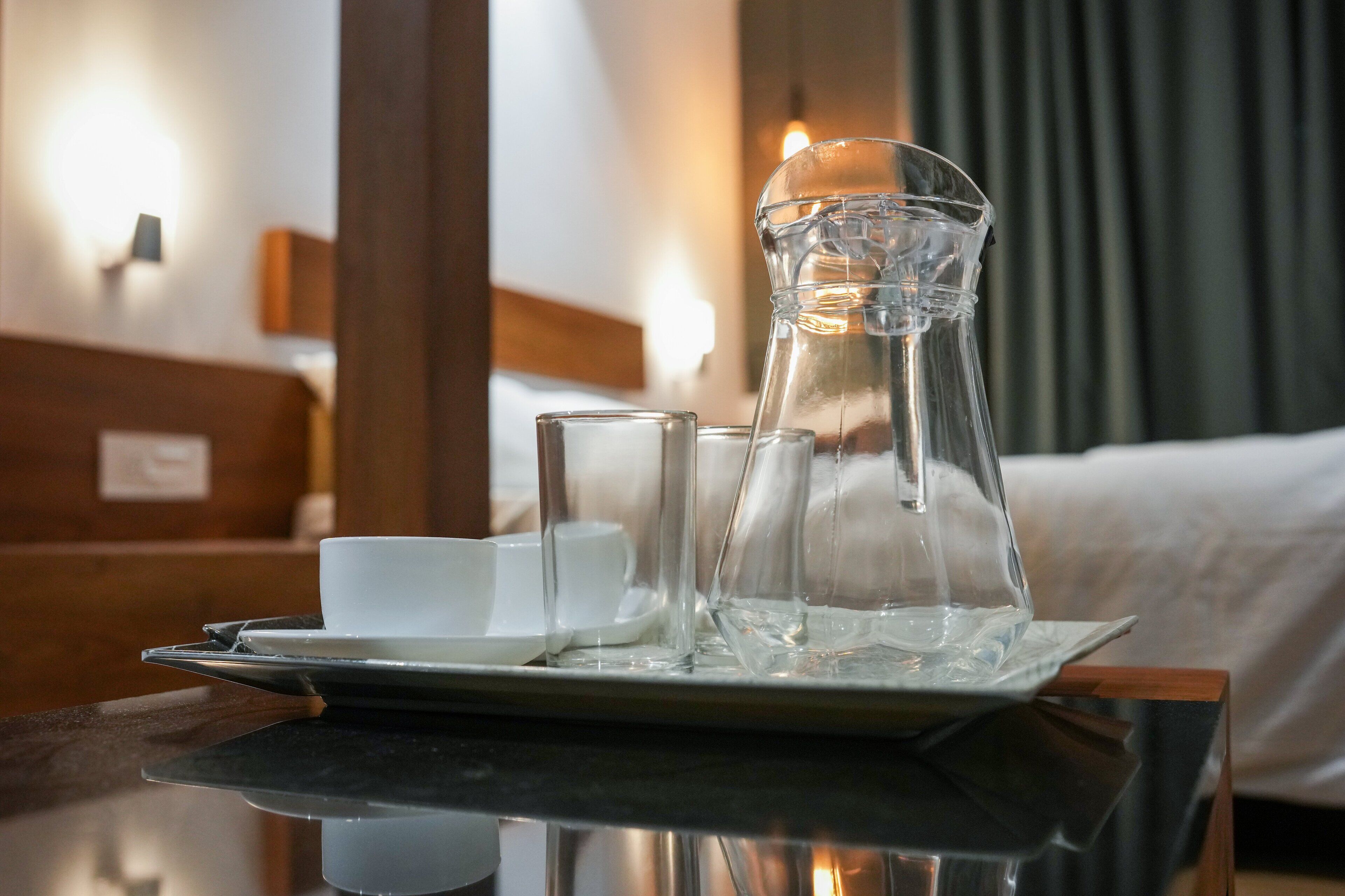 Ein Tablett mit einer Glaskaraffe, zwei Gläsern und einer Tasse auf einem Tisch in einem Hotelzimmer.