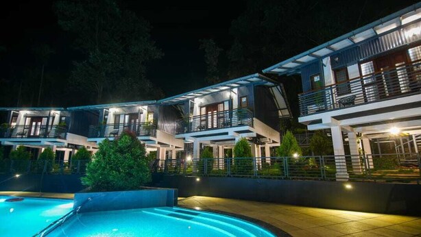 A modern hotel with multiple guest rooms, a swimming pool, and a well-lit outdoor area at night. - B'camp Resorts & Homestays (Vythiri)