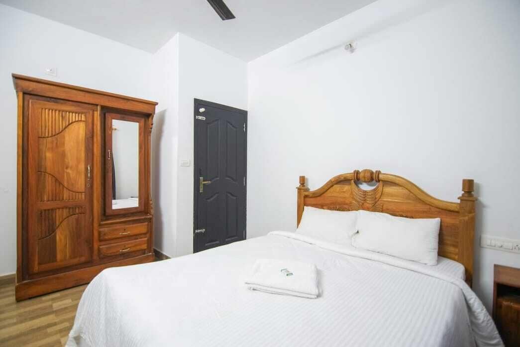 A bedroom with a wooden wardrobe, a black door, and a bed with white bedding.