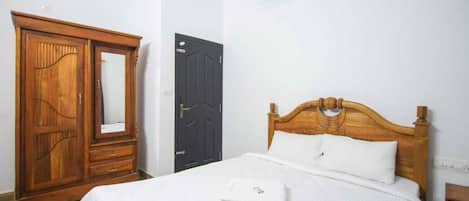 A bedroom with a wooden wardrobe, a black door, and a bed with white bedding.