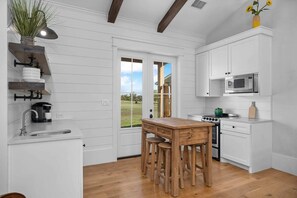 A kitchen with white cabinetry, a wooden table, stools, a sink, a stove, and a microwave.