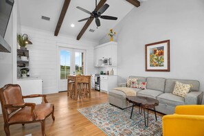 A spacious living area with a wooden floor, a ceiling fan, a gray sofa, a yellow armchair, and a dining area with wooden chairs and a table.