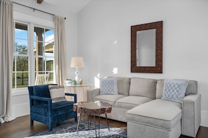 A living room with a blue armchair, a grey sofa, a round coffee table, and a large mirror on the wall.