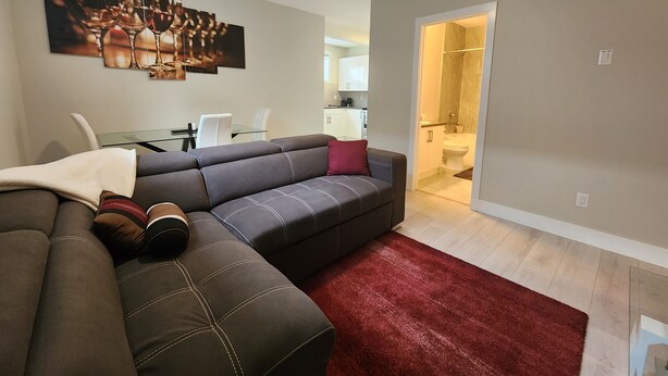 A modern living room with a sectional sofa, a red rug, and a dining area with a glass table and chairs. - Family-friendly, clean & affordable 2-BR basement suite close to YEG airport. (Edmonton)