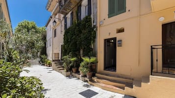 A narrow street with buildings on either side, potted plants, and a clear blue sky.