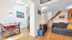 A modern living space with a dining area, a sofa, a staircase, and a painting on the wall.