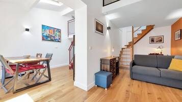 Ein moderner Wohnbereich mit Essplatz, einer Couch, einer Treppe und einem Gemälde an der Wand.