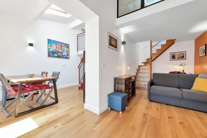 A modern living space with a dining area, a sofa, a staircase, and a painting on the wall.