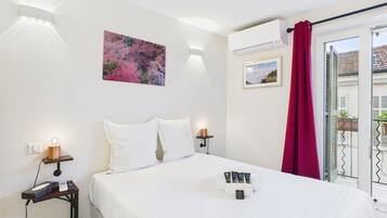Ein Hotelzimmer mit Bett, Nachttischen, einem Gemälde, einer Klimaanlage und Blick nach draußen.