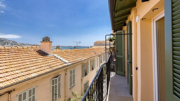 A balcony with a view of terracotta-roofed buildings and a clear blue sky.