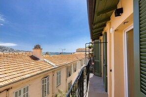Un balcon offrant une vue sur des bâtiments aux toits de tuiles rouges et un ciel d’un bleu éclatant.