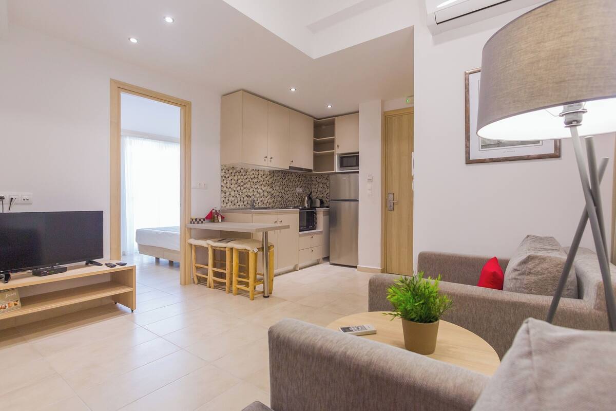 A modern living room with a flat-screen TV, a coffee table with a plant, and a sofa with a red pillow.