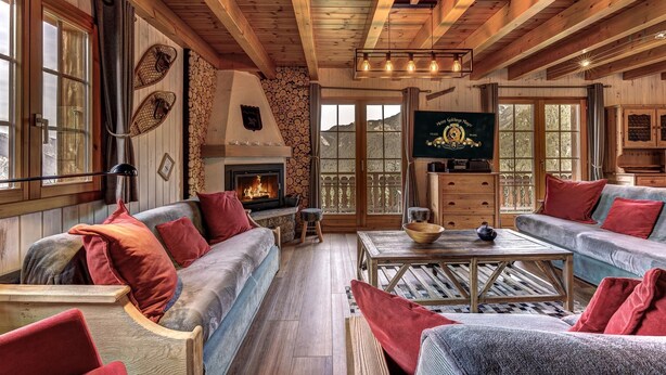 A cozy cabin interior with wooden beams, a fireplace, and a stone wall.