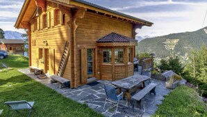 A wooden chalet with a stone patio, outdoor seating, and mountain views.