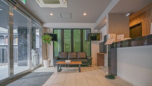 A modern reception area with a glass door entrance, a leather sofa, a wooden coffee table, and a reception desk with a flat-screen TV.