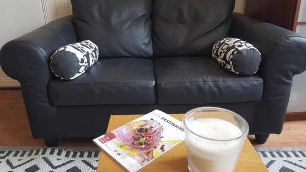 A black leather sofa with patterned cushions, a magazine, and a glass of milk on a wooden table. - Large room in historic village center with panoramic view  (Lézat-sur-Lèze)