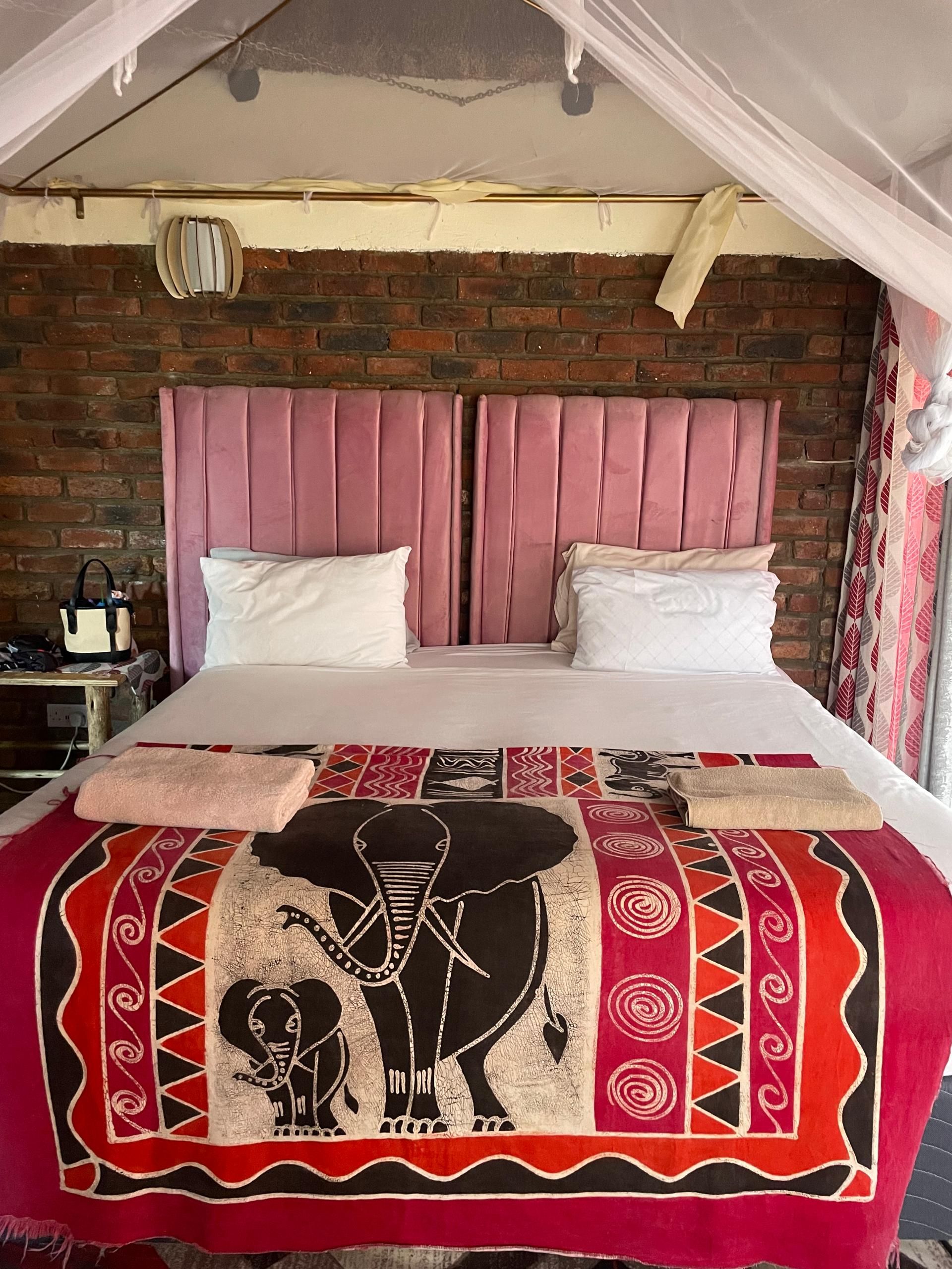 A bed with a headboard, a blanket with a large elephant design, and a brick wall behind.