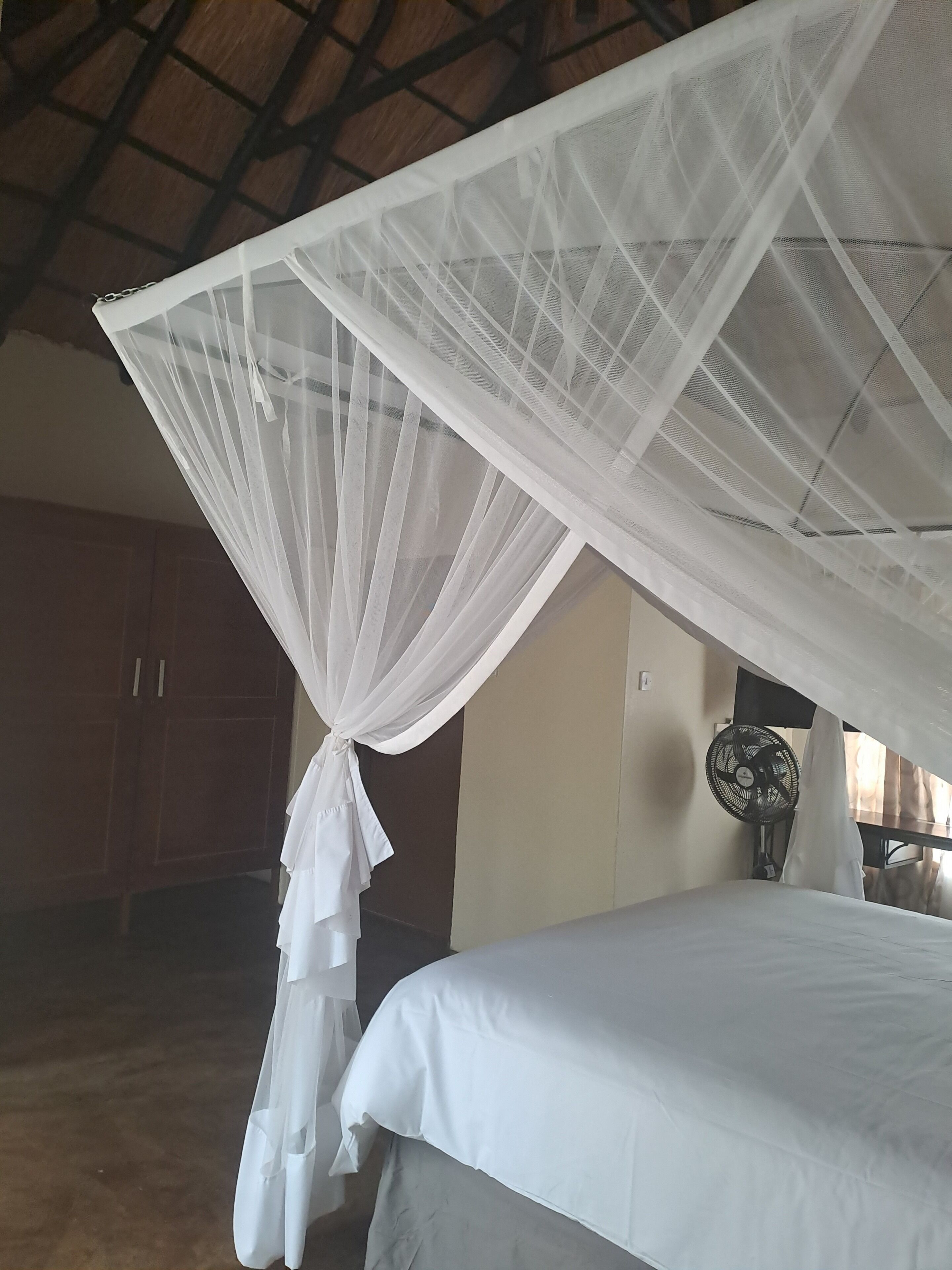 A bedroom with a bed, a mosquito net, a fan, and wooden cabinets.