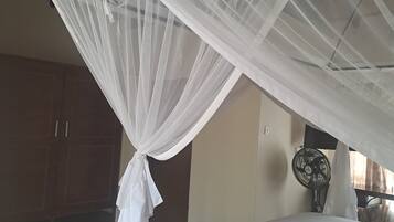 A bedroom with a bed, a mosquito net, a fan, and wooden cabinets.
