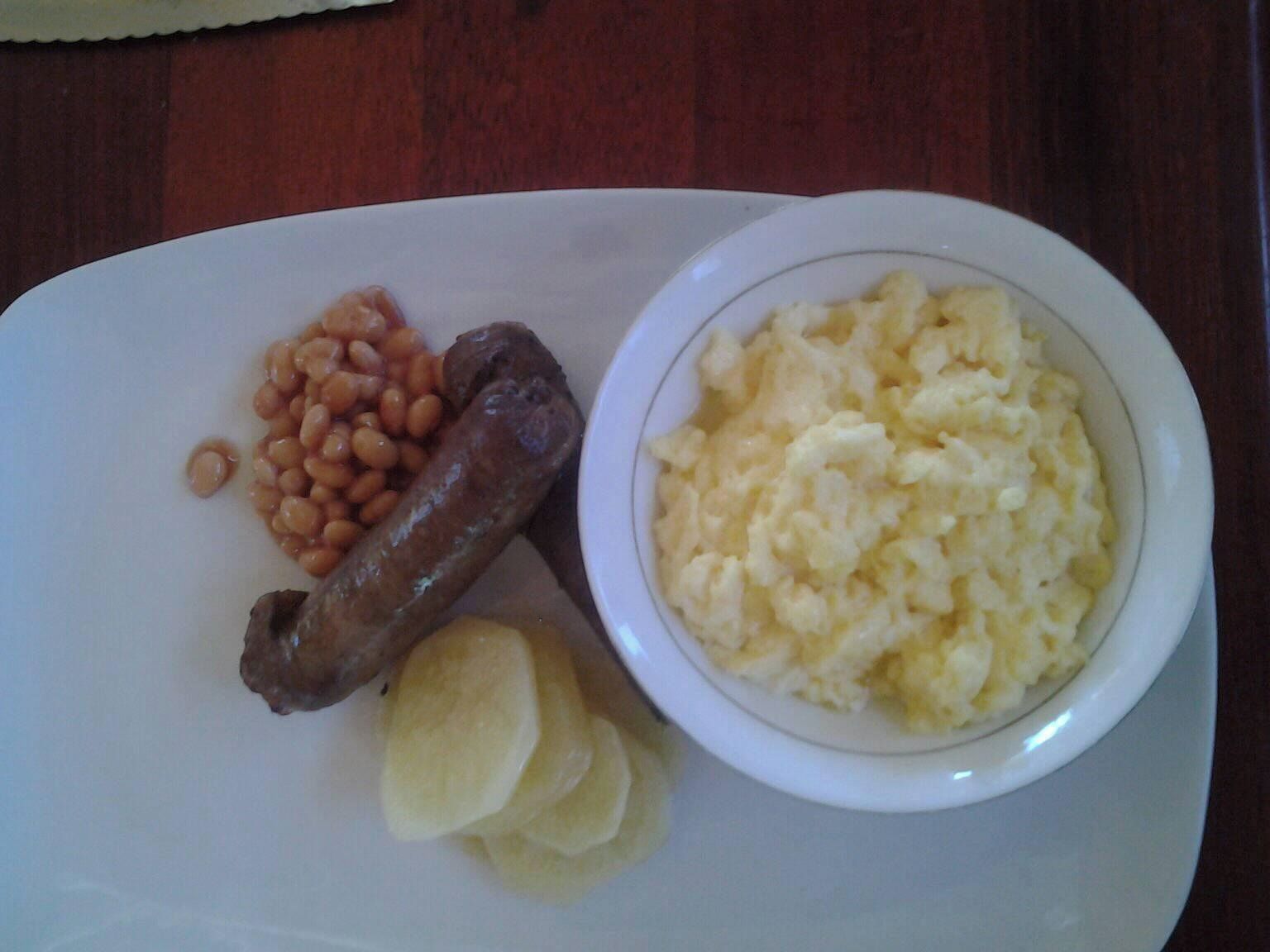Un plato con salchicha, puré de papas, frijoles horneados y una porción pequeña de papas fritas.