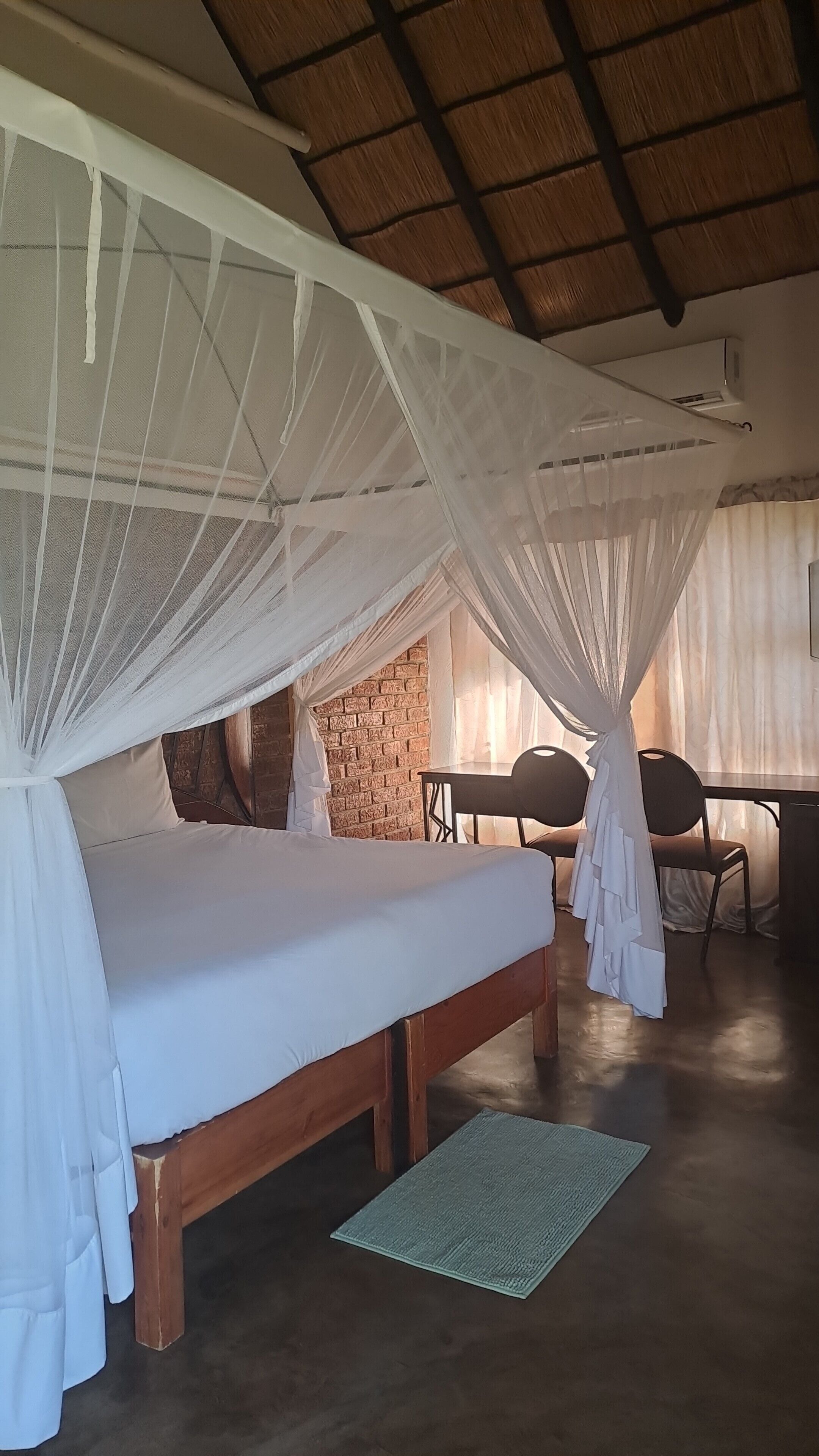 A room with a bed under a canopy, a brick wall, a table with chairs, and an air conditioning unit.