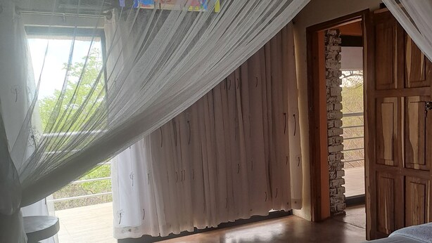 A bedroom with a bed, a small table, and a window with sheer curtains. -  iroCK Lodge (Victoria Falls)