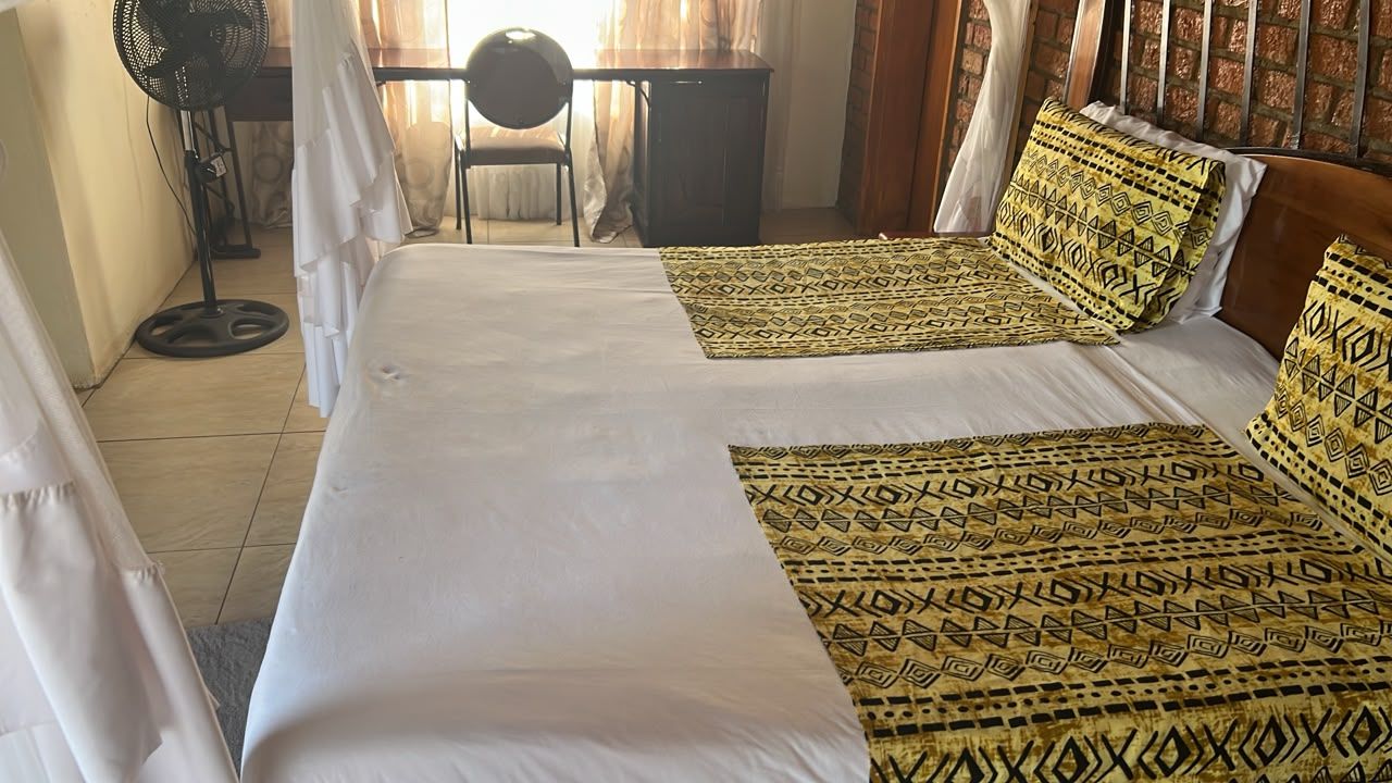 A hotel room with a bed, a desk, a chair, and a standing fan.