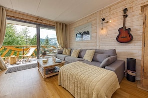 Ein gemütliches Wohnzimmer mit großem Fenster, einer Couch, einem Couchtisch und einer Gitarre an der Wand.
