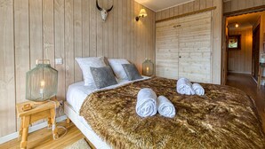 Une chambre avec un mur en bois, un lit avec une literie blanche, deux oreillers, un plaid en fausse fourrure et une paire de serviettes.