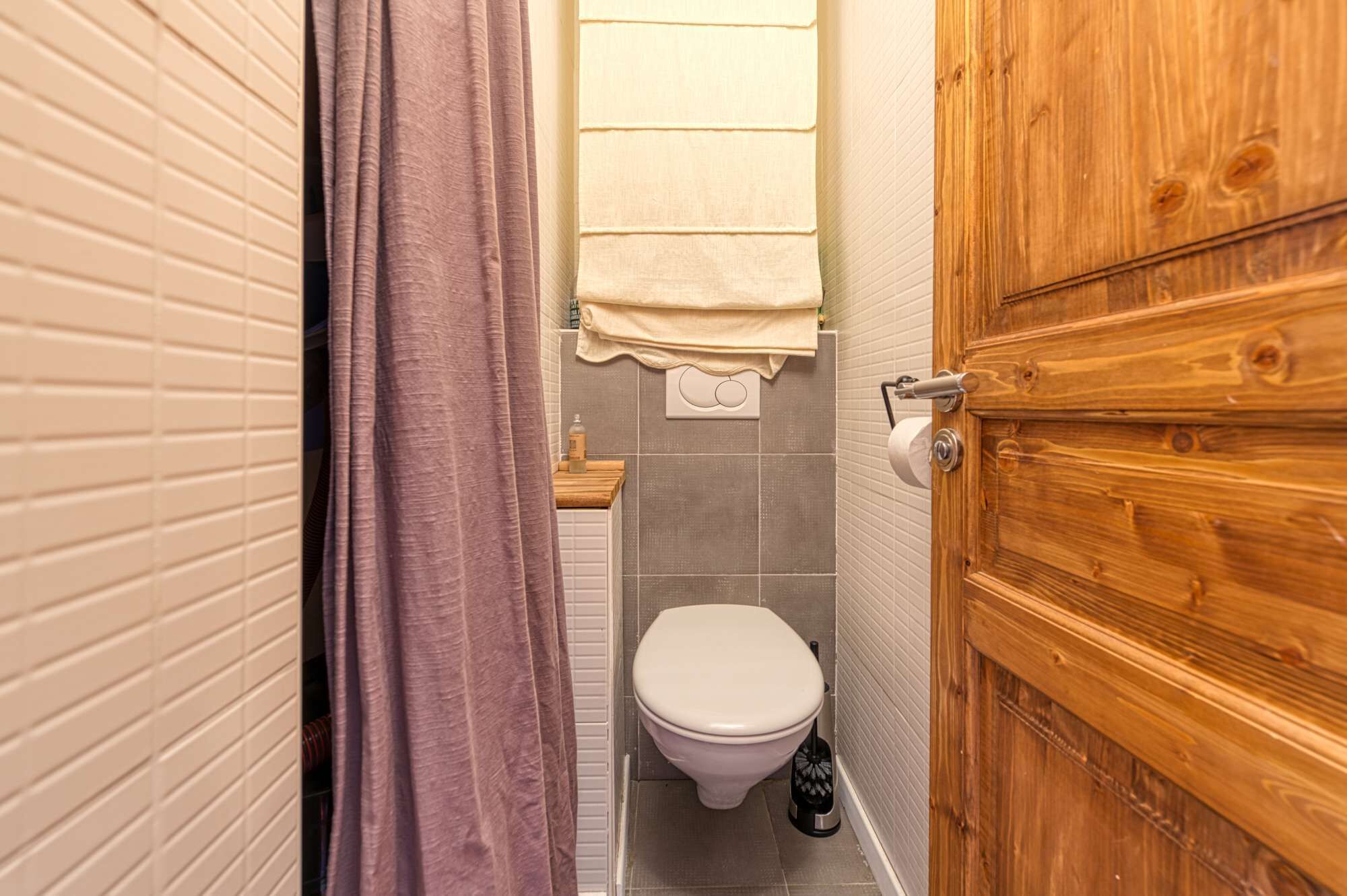 A bathroom with a wooden door, a toilet, and a shower curtain.