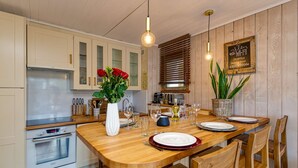 Une cuisine avec des meubles de rangement en bois, une table à manger en bois dressée pour quatre personnes et une horloge au mur.