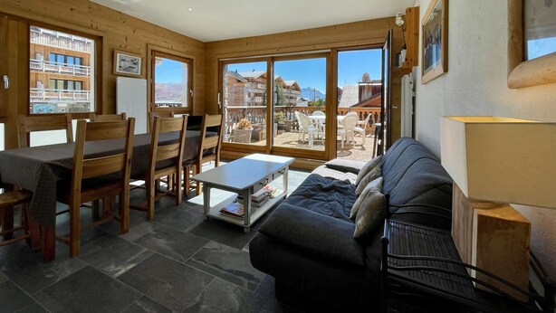 A cozy room with a bed, a sofa, a dining table with chairs, and a large window offering a view of a mountain and buildings. - Résidence la Ménandière W1 (Alpe d'Huez)